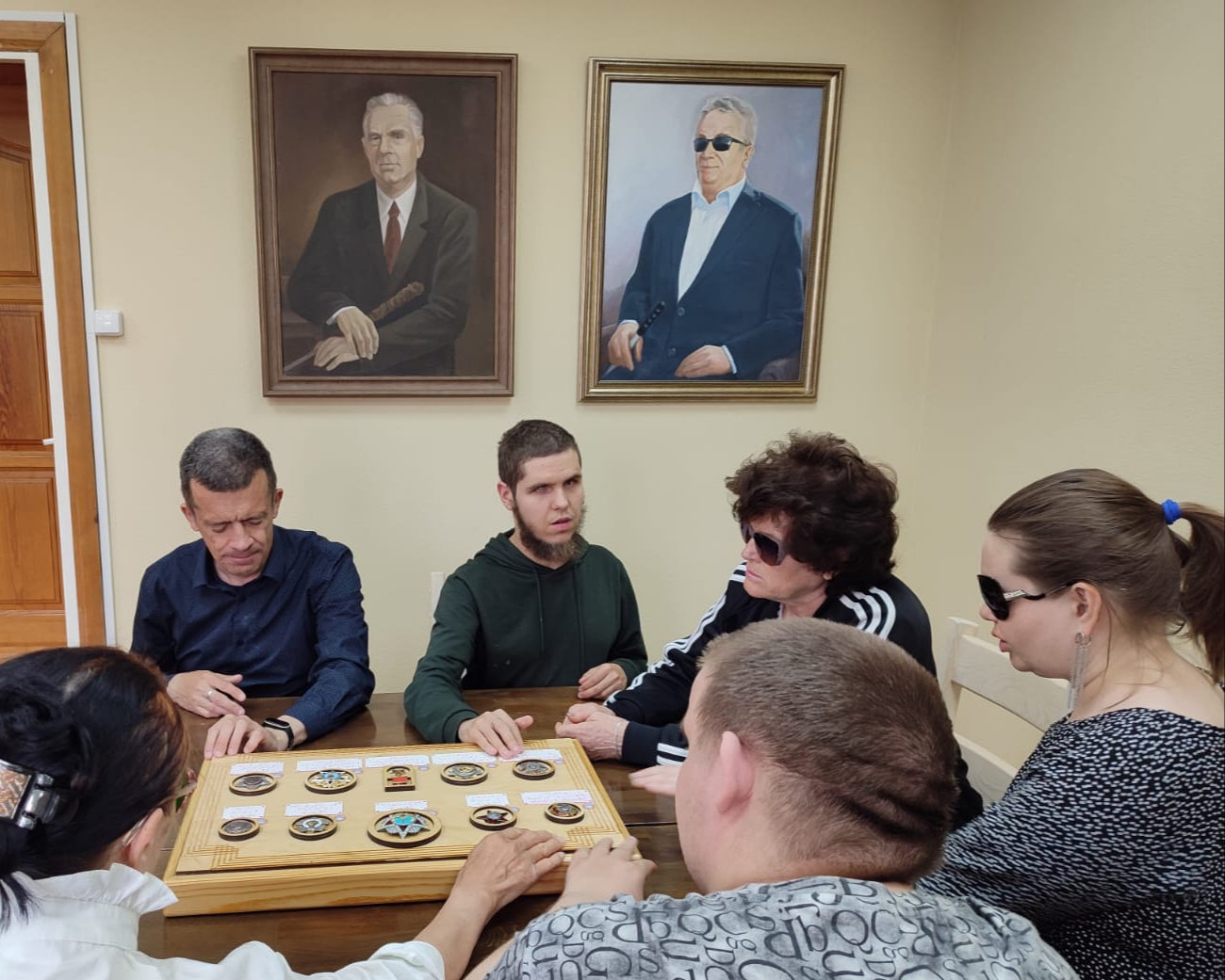 Тифлокомментарий к фотографии: учащиеся Бийского филиала ЦРС ВОС в Музее на фоне портретов Михаила Никитовича Наумова и Анатолия Макаровича Астанина изучают экспозицию "Ордена и медали".