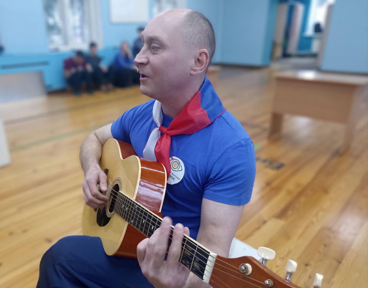 Тифлокомментарий к фотографии: На фото крупным планом изображен мужчина с гитарой в руках, он исполняет песню.