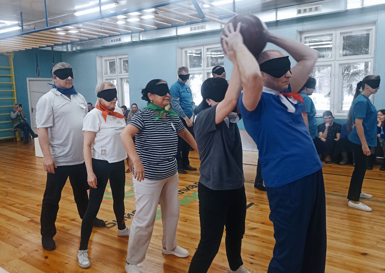 Тифлокомментарий к фотографии: В спортивном зале Бийского филиала ЦРС ВОС участники команды стоят друг за другом,  руки первых двух людей подняты вверх, они передают друг другу большой мяч, остальные в ожидании  мяча.