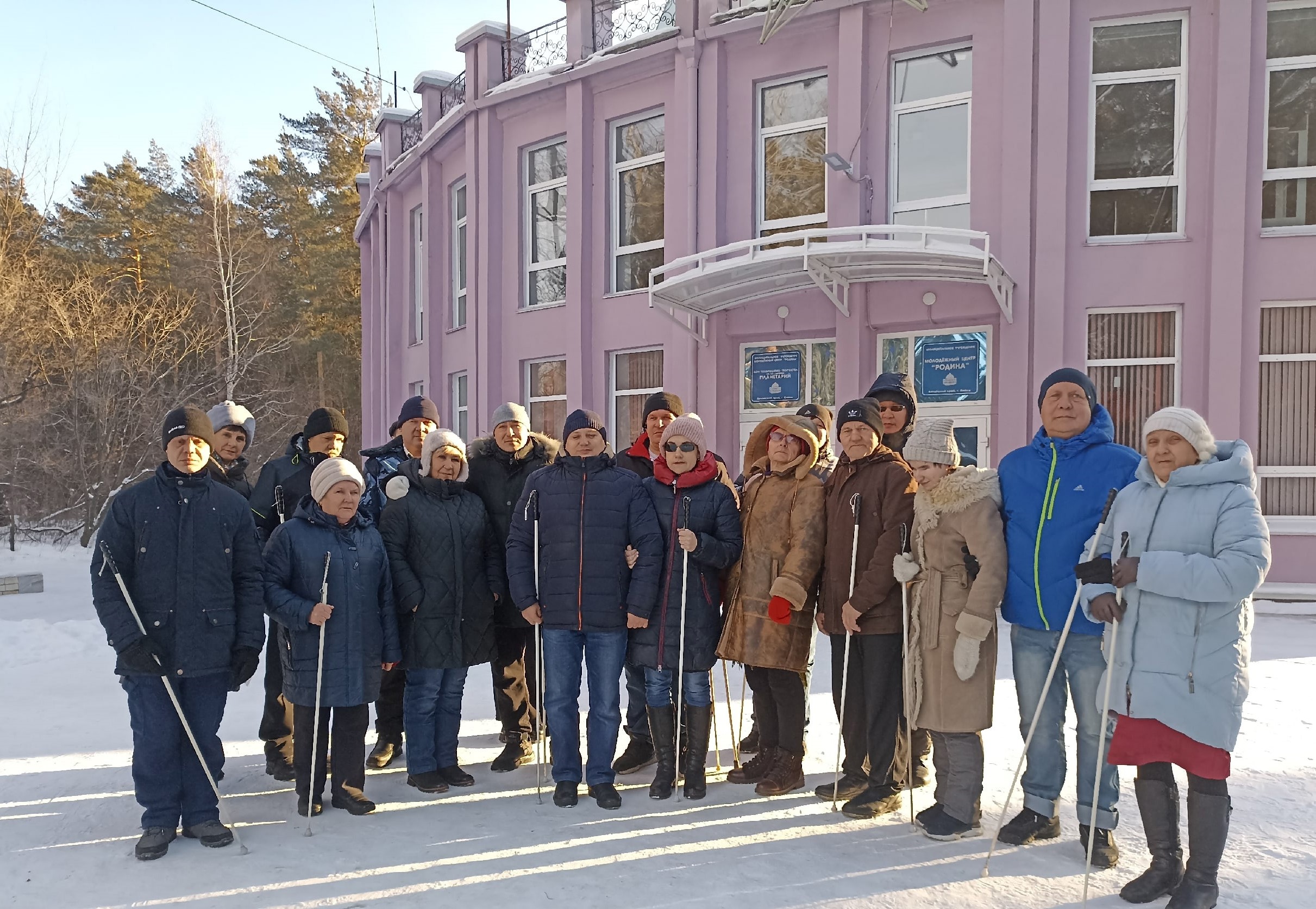 Тифлокомментарий к картинке: групповая фотография участников экскурсии в Бийский планетарий. Морозный зимний день, тепло одетые обучающиеся Бийского филиала ЦРС ВОС стоят на фоне розового здания Бийского планетария.